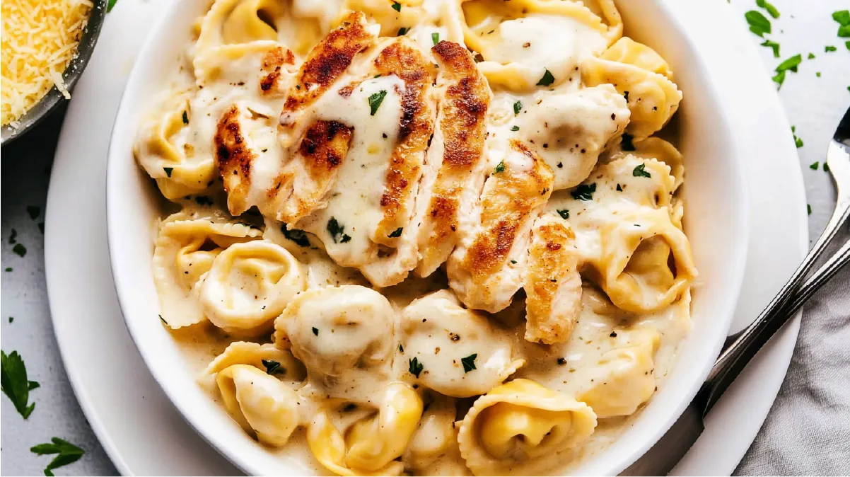 A bowl of Chicken Tortellini Alfredo Olive Garden style topped with grilled chicken slices and creamy sauce.